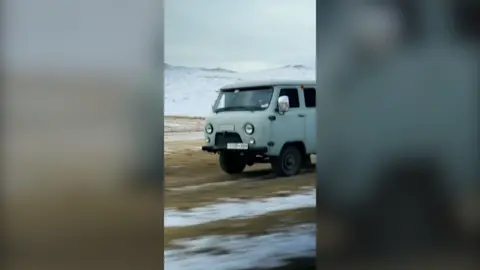 A green camper van moving down a mountain. 