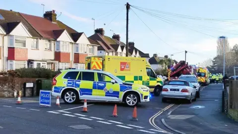 Eddie Mitchell A police car, two ambulance and a highway assistance vehicle are on a road. People in high vis clothing are visible in the background, and traffic cones block the entrance to the road. 