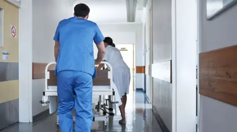 Rearview shot of hospital staff wheeling a patient in a gurney down a corridor