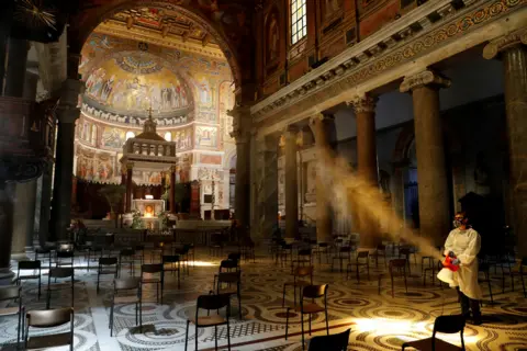 Remo Casilli / REUTERS A man disinfects Rome's Basilica di Santa Maria in Trastevere