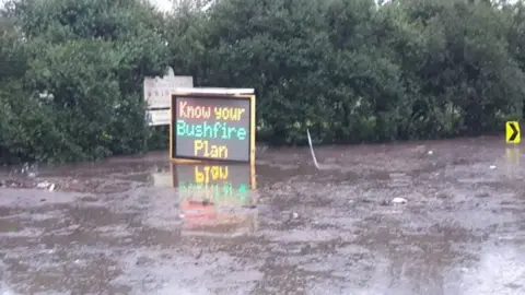 MATTHEW BENNETT Flood waters lap a bushfire warning road sign