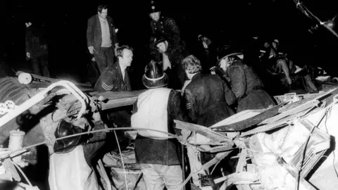 Walter Bloxham/Warwickshire Police/Nuneaton Memories Emergency workers in a black and white photo amid the wreckage. Some wear helmets while some are bareheaded.