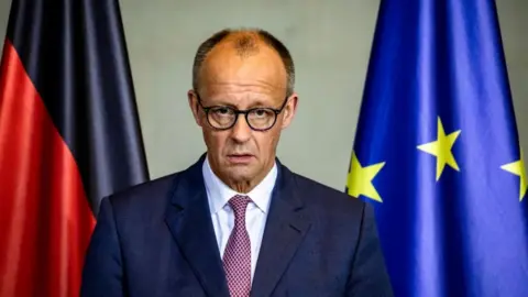German Chancellor Friedrich Merz wearing a suit in front of an EU flag and a German flag