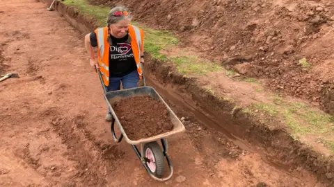 A woman pushing a wheelbarrow full of dirt