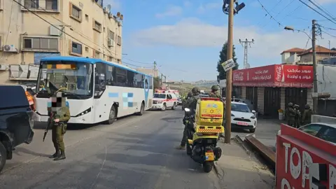 Israeli soldiers and paramedics at the scene of a deadly shooting attack on a bus and other vehicles in the village of al-Funduq, in the occupied West Bank (6 January 2025)