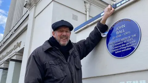 Blue Plaques St Albans Tim Boatswain standing next to a blue plaque that has been unveiled to John Ball the leader of the Peasants' Revolt in 1381