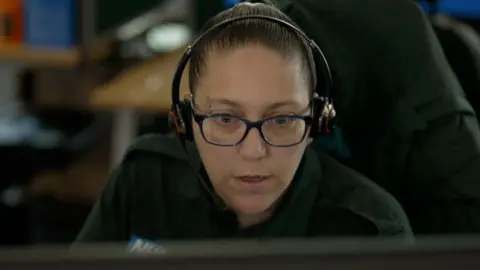 A female ambulance call handler with a headset staring at a computer screen 