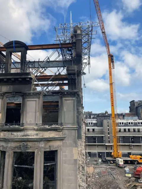City of Edinburgh Council A fire damaged old building with parts of the wall supported by scaffolding and a large yellow crane at one side