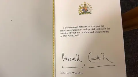 A card which says "it gives us great pleasure to send you our sincere congratulations and special wishes on the occasion of your one hundred and sixth birthday on 25th April, 2026. The King and Queen have also signed the card and it has Mrs Hazel Whittaker on the card. 