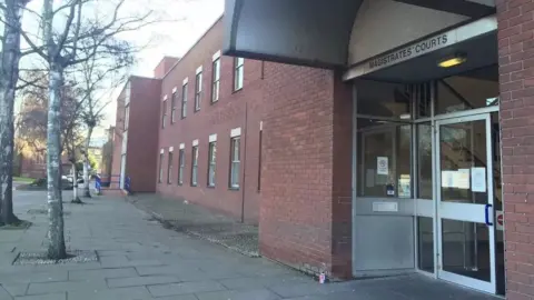 The outside of Ipswich Magistrates' Court - a red brick building with a silver/metal door with glass windows