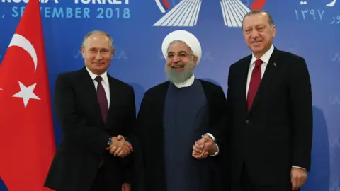 Anadolu Agency Vladimir Putin, Hassan Rouhani and Recep Tayyip Erdogan shake hands at a summit in Tehran, Iran (7 September 2018)