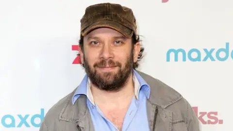 Isa Foltin/Getty Images A man with a beard and a brown cap stares at the camera