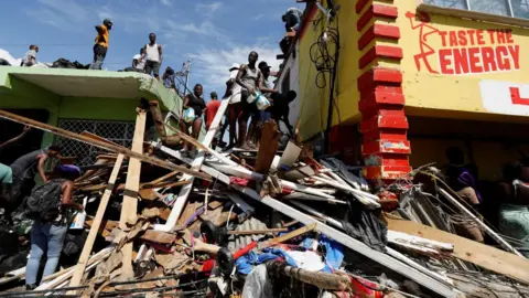 Men stand atop rubble beside a brightly-painted building