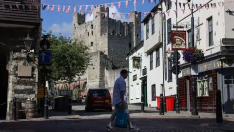 Rochester Castle in the background looking down Rochester High Street. It is a sunny day.  