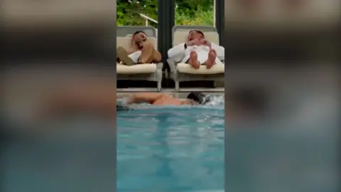 Two men chatting on sun loungers beside an indoor swimming pool