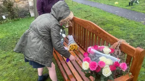 Rob Clark Ali and Rob Clark's daughter places flowers on a memorial bench outside St Mary's Church, Elloughton