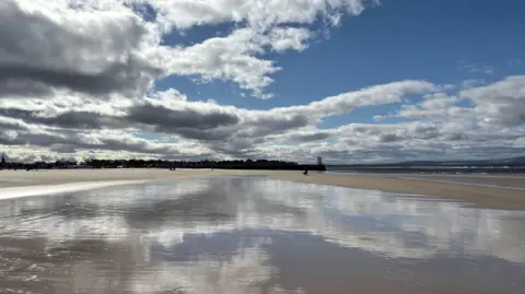 Rob Ware A beach with the blue sky and clouds reflected on the water
