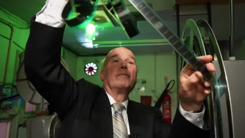 A man holding up and examining some film negatives from a projection reel