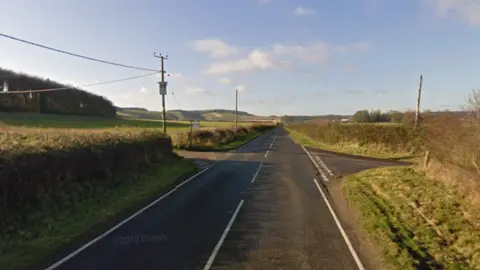 A crossroads on a straight section of the A30. One side road is a farm track and the opposite side road is a country lane.