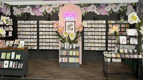 Lola Design A stand at an exhibition featuring Lola Design's work at an. Many greetings cards are displayed in rows.