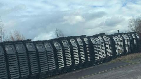 Row of dozens of new wheeled bins stacked up