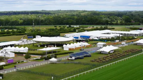 Royal Ascot A picture of Royal Ascot with gazebos and shelters placed around and next to the race track.
There are a lot of trees in the background with the racetrack in the foreground.