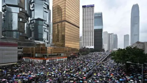 Getty Images Protesters shelter under umbrellas during a downpour as they occupy roads near the government headquarters in Hong Kong on June 12, 2019.