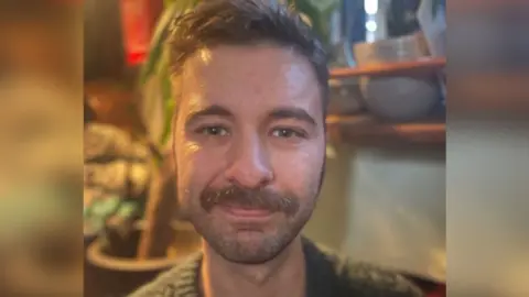 A man with a moustache looks into the camera from inside a houseboat