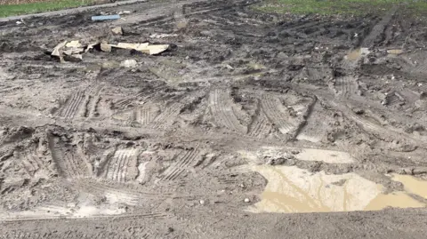 A picture of grass turned into mud with tyre tracks all over it