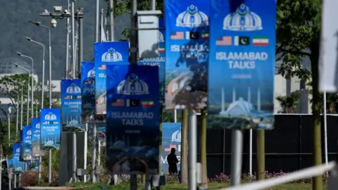 A silhouetted man stands next to advertisement posters reading “Islamabad Talks” at the Convention Centre in Islamabad, Pakistan
