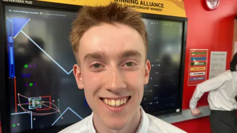 Aaron smiling at the camera. He has light brown hair and is wearing a white shirt.