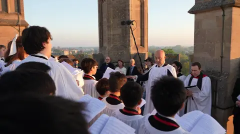 Choristors in white gowns sing from atop Magdalen Tower.