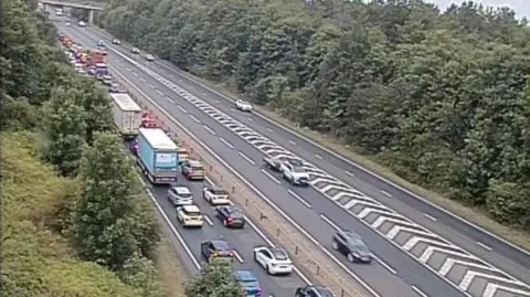 The A14, showing cars queuing on one side of the road, and cars driving on the other side. There are trees either side of the road. 