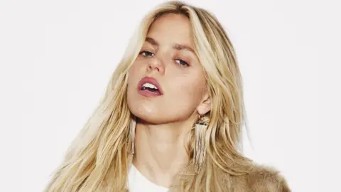 Pop star Renée Rapp poses against a white backdrop. Her lips are parted and her expression suggests defiance