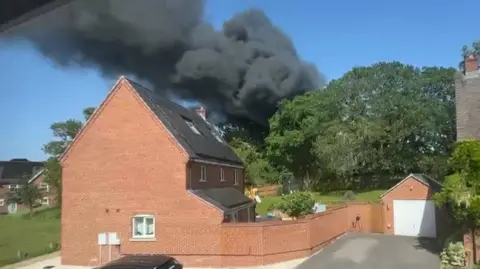 Dark smoke seen rising over a large red brick home.