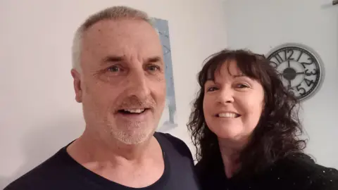 Victoria Kidd A man and a woman smiling into the camera with a clock behind them hanging on a white wall