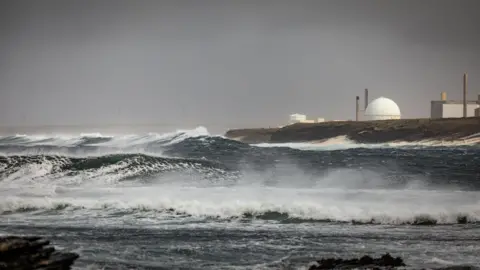 Getty Images A view of the Dounreay nuclear power over waves crashing on the shore below. Dounreay is made up of a number of buildings, including its distinctive "golf ball", a spherical structure housing a nuclear reactor.