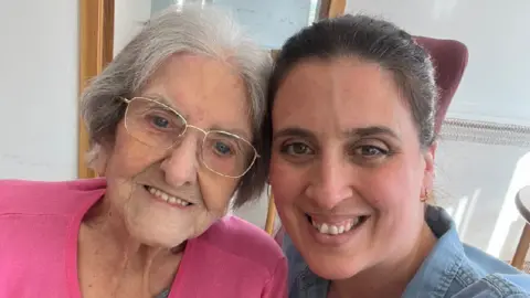 Beca Lyne-Pirkis Seflie of Beca Lyne-Pirkis with her grandmother. Beca is on the right and her grandmother is on the left. Both are smiling looking at the camera. Her grandmother wears a pink top, has greying-white hair and thin-rimmed glasses. Beca has a blue top on. It is a head and shoulders shot of them.