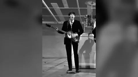 A black and white photo of Paul McCartney playing his bass in the 19060s