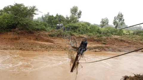 Reuters A man crosses a flooded Umvumvu river in Chimanimani, Zimbabwe - 18 March 2019