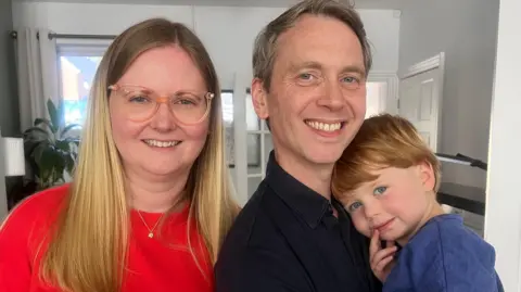 BBC A mum, dad and two year old boy smiling at the camera.