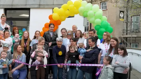 Cumberland Council A large group of people are standing under an archway made of balloons while a woman cuts a ribbon. 