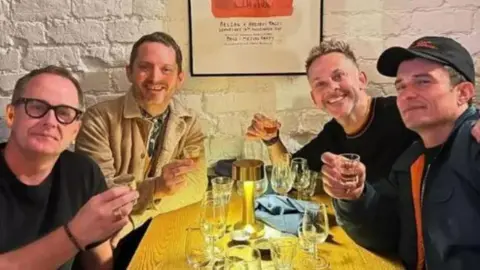 Dominic Monaghan (L-R) Billy Boyd, Elijah Wood, Dominic Monaghan and Orlando Bloom sit around a table in a restaurant, holding shot glasses 