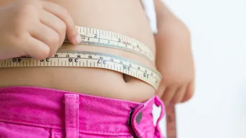 Getty Images Girl measuring her waist with a tape