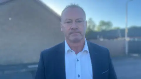 A man with a white shirt, blue jacket and short hair