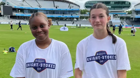 Two girls wearing white T-shirts with the competition logo on, saying "KNIGHT-STOKES CUP"