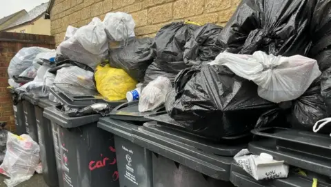 Piles of bin bags dumped on top of over flowing wheelie bins 