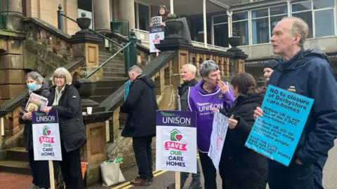 People with protest placards stood outside stone steps 