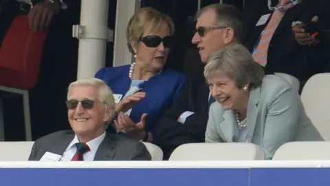 Getty Images  Sir Michael Parkinson sat in the front row of a seated area at Lord's, with Theresa May sat behind him, them both laughing. Mrs May's husband Philip is sat to her right 