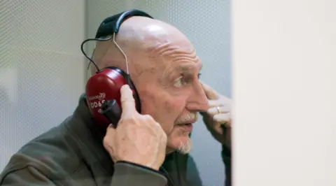 Ian Holloway points to his head while wearing headphones.
